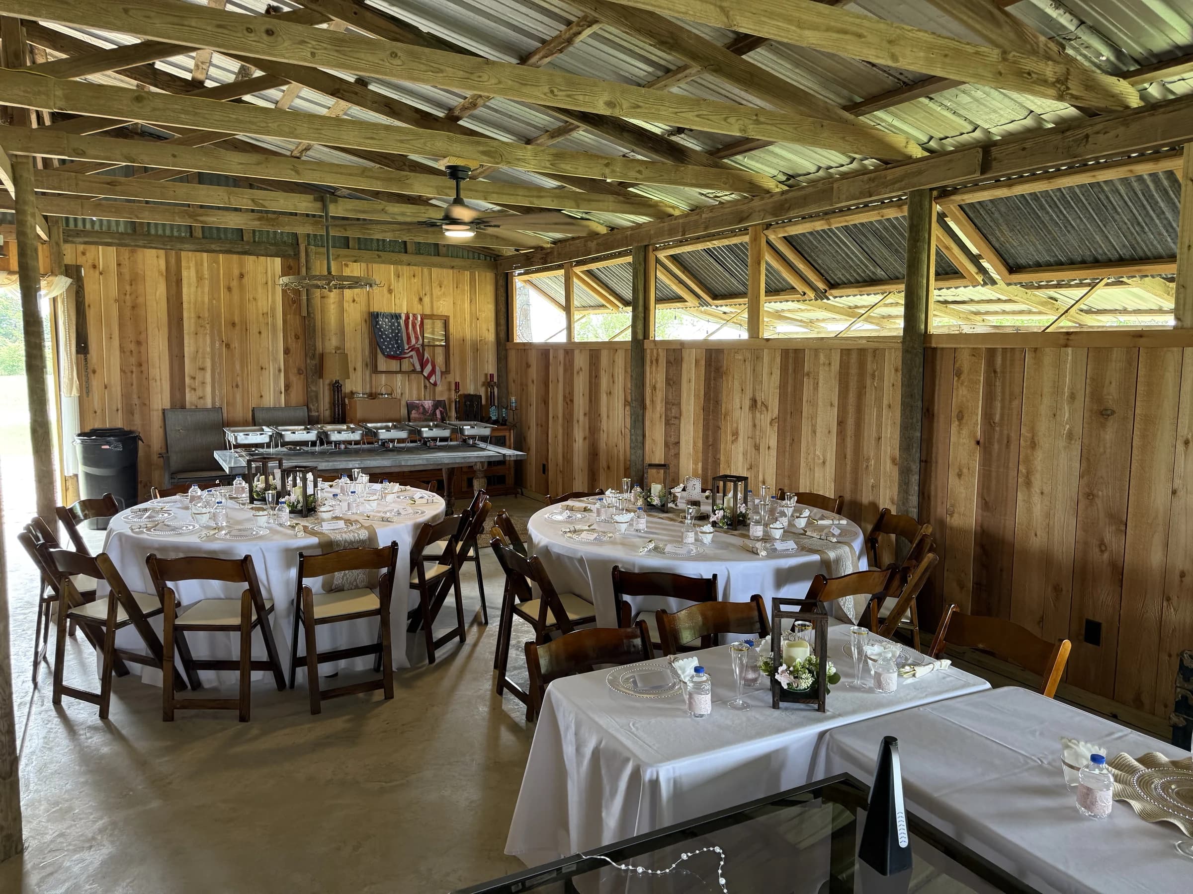 White-linen reception tables and wooden chairs beneath the barn’s exposed roof beams