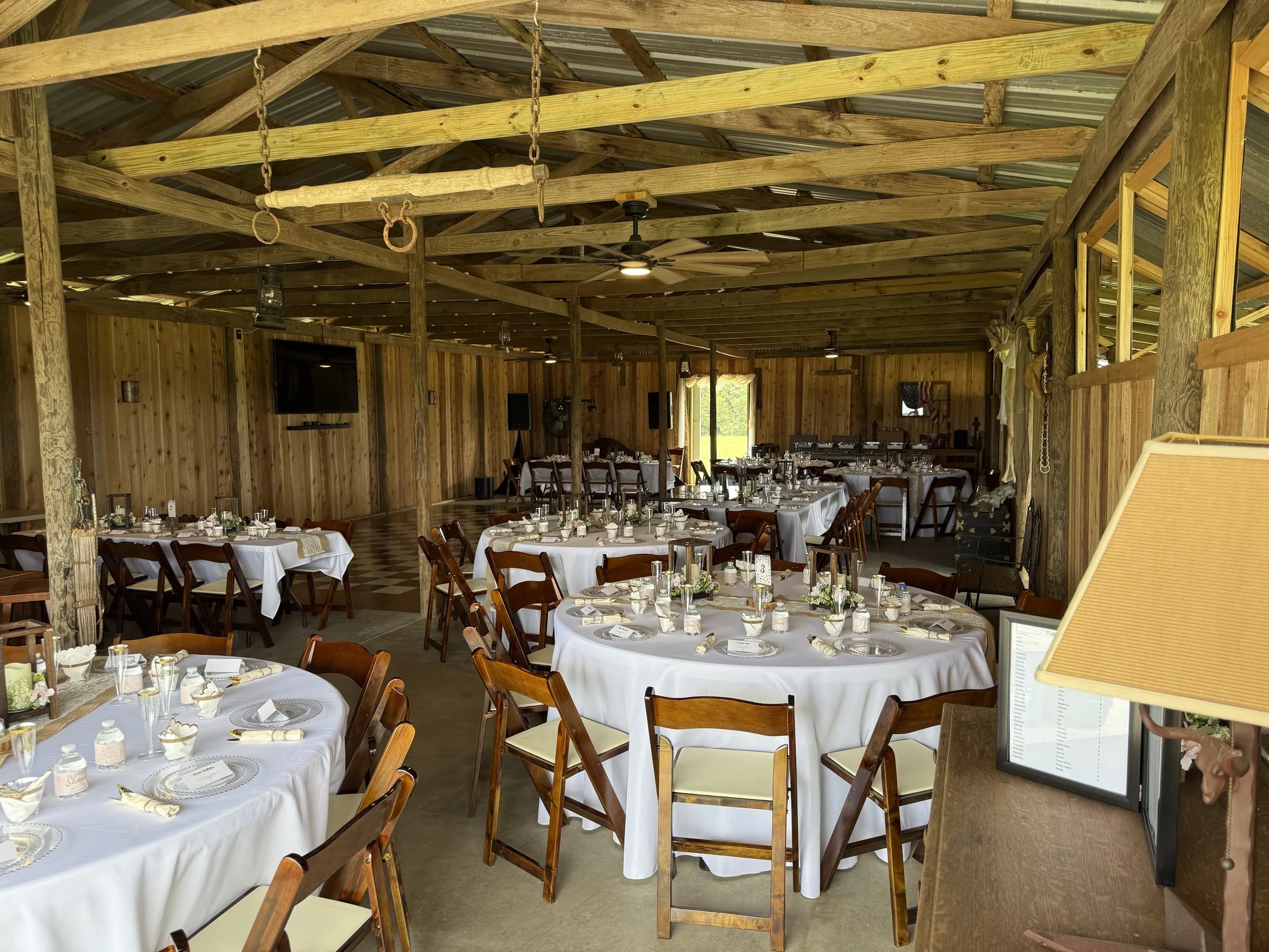 Rows of reception tables with white linens, place settings, and wooden chairs inside the barn