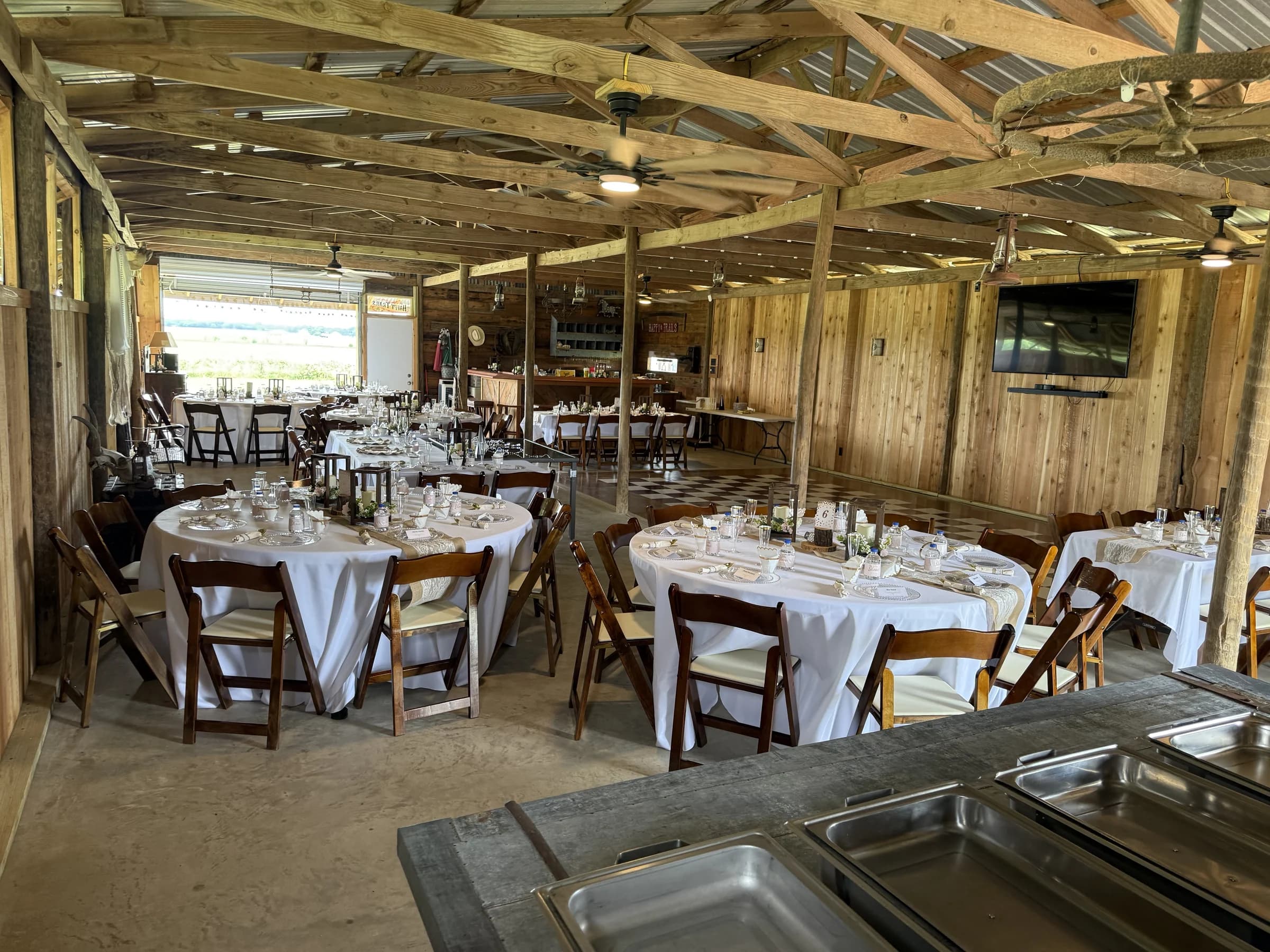 Round reception tables set with white linens beneath exposed wooden beams