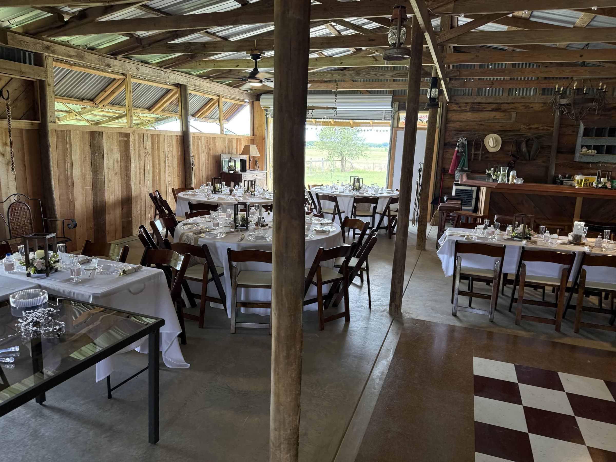 Tables set with white linens inside the timber barn, with the custom bar beyond