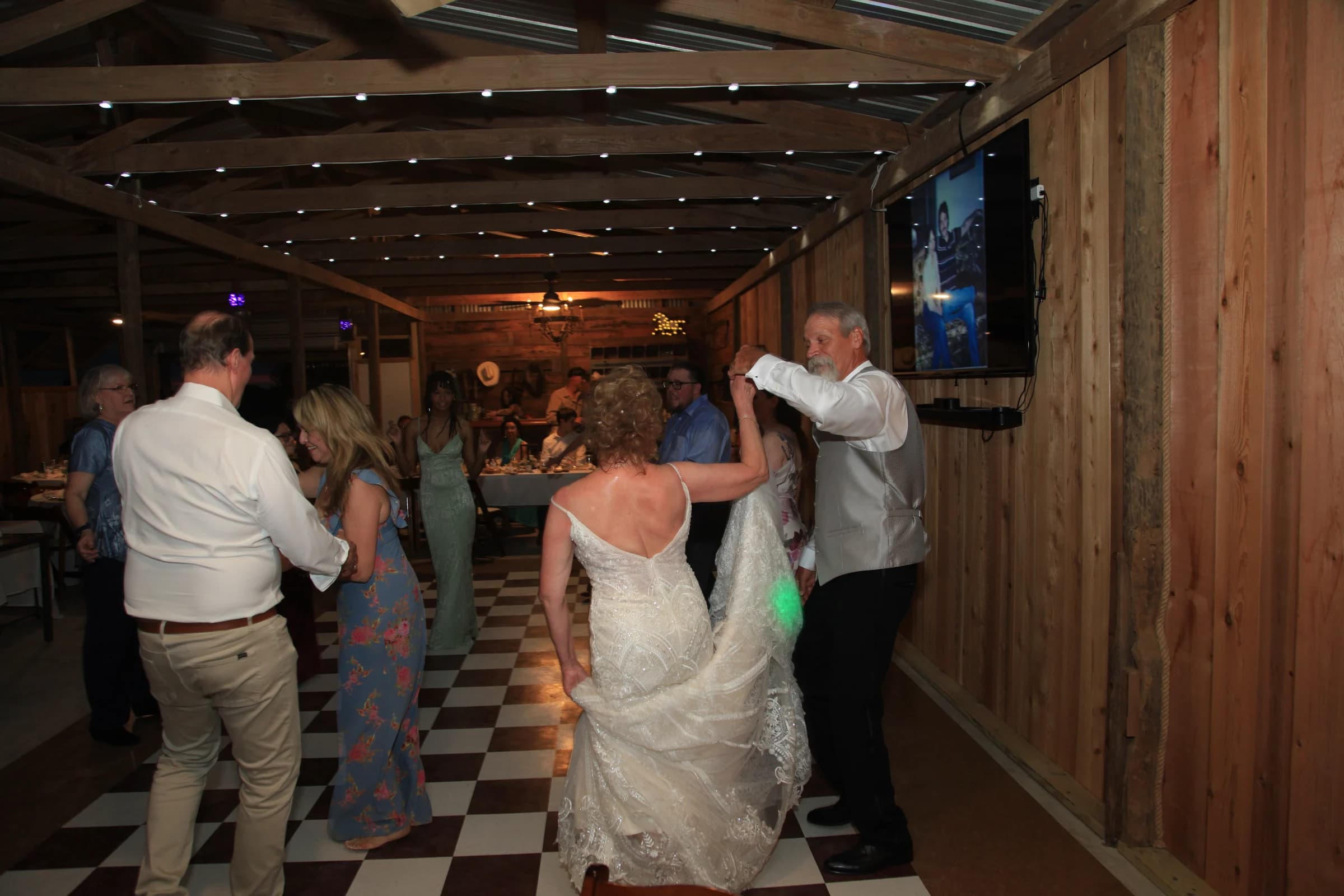 A bride and wedding guests dancing in the barn under warm string lights
